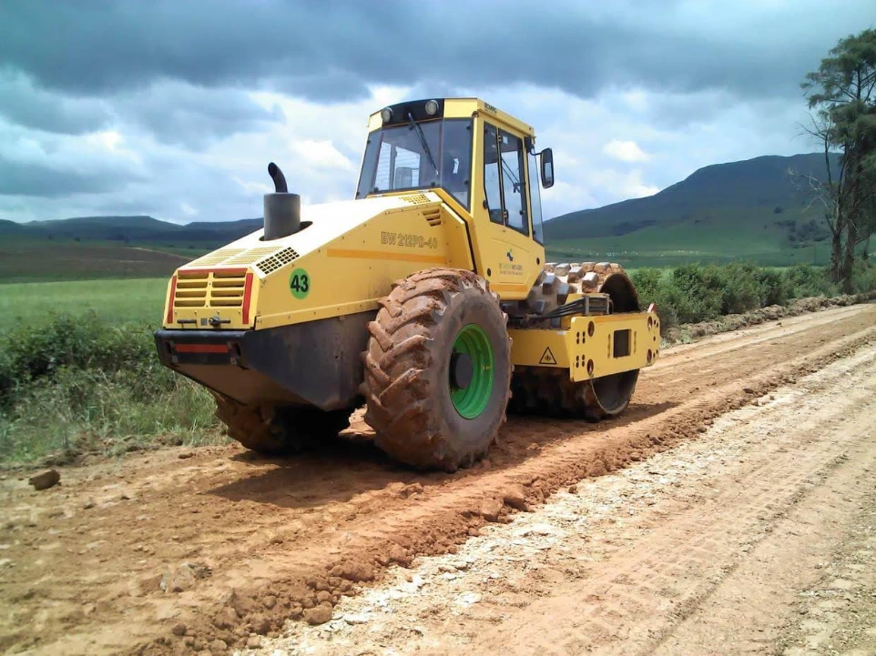 Trust Partners Geo-Group active road works site featuring heavy machinery, including graders and asphalt pavers, improving road infrastructure. Workers ensure quality and safety while enhancing transportation routes in Kenya